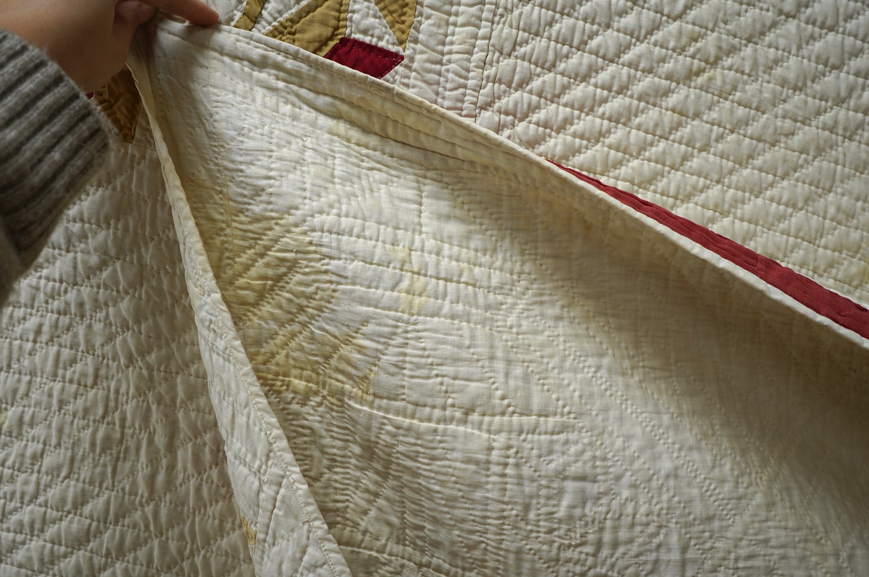 An early 20th century American ‘Carolina Lily’ quilt, worked on a cream cotton in two colours, sand and red patchwork creating motifs of large angular abstracted vases of flowers, the quilt then bordered with red, 185cm